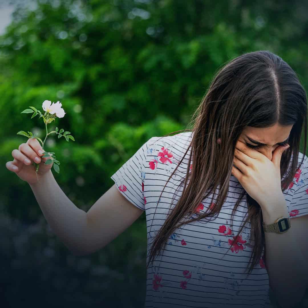 κοπέλα με αλλεργίες, κρατάει ένα λουλούδι και τσούζουν τα μάτια της